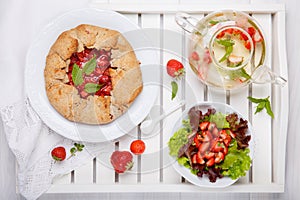 Strawberry galette, summer fruit salad and herb tea. Homemade healthy wholegrain berry open pie. Fruit tart. Top view