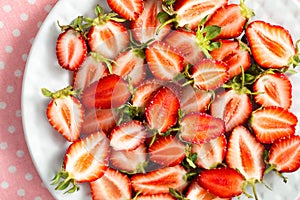 Strawberry halves spread out on a white plate. Red juicy berries with green sepals