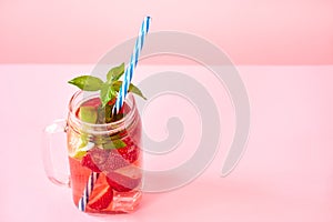 Strawberry homemade lemonade in a mason jar with copy space on pink background.