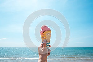 Strawberry ice cream in a wafer cone sticking out held in woman`s hand with tropical beach background
