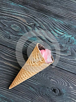 Strawberry ice cream in a waffle cone. Against the background of pine brushed boards painted in black and green