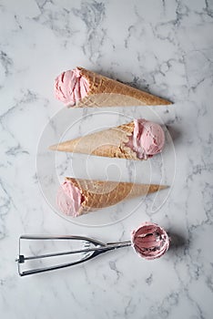 strawberry ice cream and waffle cone on marble background, top view