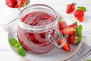 Strawberry jam in the glass jar with fresh berries on a white wooden table. Summer dessert. Copy space