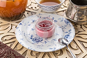 Strawberry jam in a jar and cup of black tea on oriental wooden table