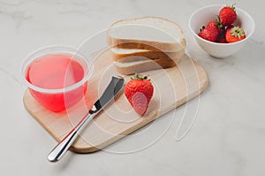 Strawberry jam. Making sandwiches with strawberry jam. Bread and strawberry jam on a white table with jar of jam and fresh