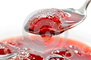 Strawberry jam is stirred with a spoon on a white background.