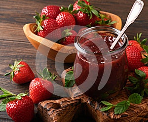 Strawberry jam. Strawberry jam in glass jar with fresh berries plate on an old wooden dark table background, closeup. Homemade str