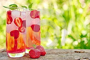 Strawberry lemonade, cocktail with ice and mint in glasses green background outdoors.