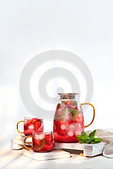 Strawberry lemonade in jug and two glass glasses. Summer drinks season. Strawberries with mint and ice cubes. Soft drink