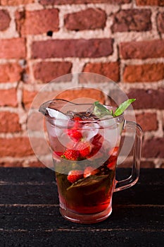Strawberry lemonade with mint and ice in a jug on a brick background