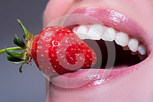 Strawberry in lips. Red strawberry in woman mouths close up. Closeup of smile with white healthy teeth.