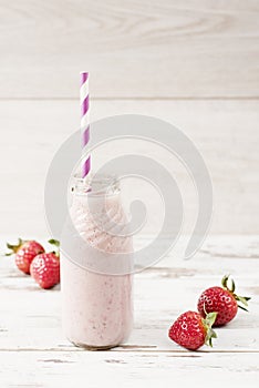 Strawberry milk in glass bottle with straw on old vintage wooden background