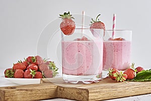 Strawberry milk shake in glass with straw and fresh berries on a white background