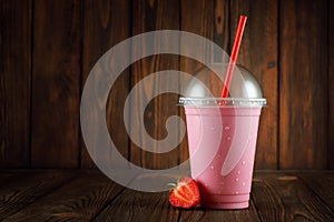 strawberry milkshake in disposable plastic glass with straw on table