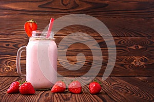 A strawberry milkshake in a mason jar. Pink smoothie on a wooden background. A yogurt with a straw and fresh berries. Copy space.