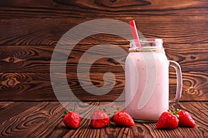 A strawberry milkshake in a mason jar. Pink smoothie on a wooden background. A yogurt with a straw and fresh berries. Copy space.