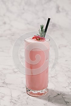 Strawberry milkshake with rosemary on white marble background.