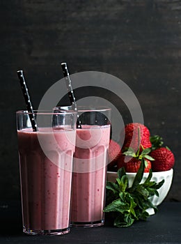 Strawberry and mint smoothie in tall glasses, bawl of fresh berries on dark rustic wood background