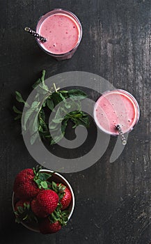 Strawberry and mint smoothie in tall glasses, bawl of fresh berries on dark rustic wood background