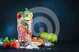 Strawberry Mojito cocktail drink with lime, white rum, soda, cane sugar, mint, and ice in glass on deep blue background. Summer