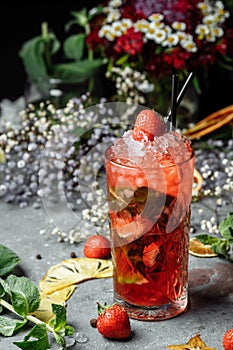 Strawberry Mojito. Cold summer mojito cocktail with strawberries, mint, lemon and ice in a glass on a table. on a dark background