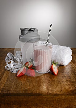 Strawberry orange milkshake, ingredients, tape measure, towel  and shaker with paper straw on a wooden table top