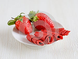 Strawberry pastille made from pure fruits in rolls and fresh berries on white plate.