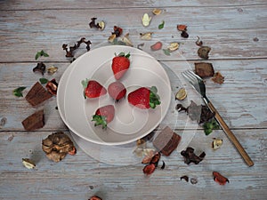 Strawberry plate with wooden fork on vintage white table with dry leaves