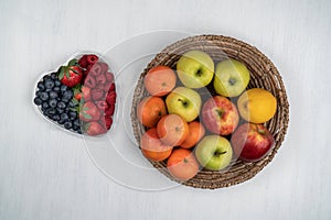 strawberry, raspberry, blueberry and a basket with apples and tangerines on a white table, top view, copy space