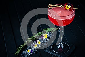 Strawberry red margarita alcoholic cocktail with tequila, liqueur and vermouth decorated with flowers on black
