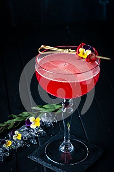 Strawberry red margarita alcoholic cocktail with tequila, liqueur and vermouth decorated with flowers on black