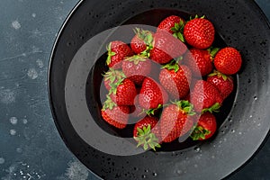 Strawberry ripe. Fresh red strawberry in black plate or bowl on dark stone background with copy space. Top view. Mock up