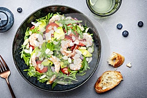 Strawberry, shrimp and herbs healthy salad with arugula, avocado and almond slices, gray kitchen table. Fresh useful dish for