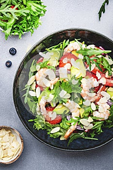 Strawberry, shrimp and herbs healthy salad with arugula, avocado and almond slices, gray kitchen table. Fresh useful dish for