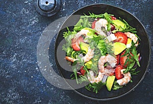 Strawberry, shrimp and herbs healthy salad with arugula, avocado and onion, blue kitchen table. Fresh useful dish for healthy