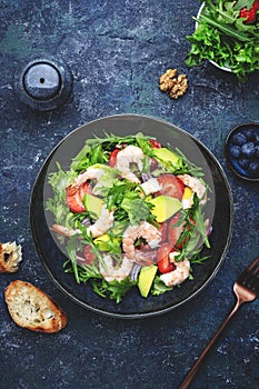 Strawberry, shrimp and herbs healthy salad with arugula, avocado and onion, blue kitchen table. Fresh useful dish for healthy