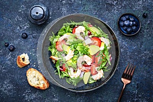 Strawberry, shrimp and herbs healthy salad with arugula, avocado and onion, blue kitchen table. Fresh useful dish for healthy