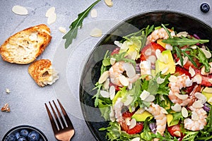 Strawberry, shrimp and herbs salad with arugula, lettuce, avocado and almond slices, gray table. Fresh useful dish for healthy