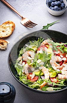 Strawberry, shrimp and herbs salad with arugula, lettuce, avocado and almond slices, gray table. Fresh useful dish for healthy