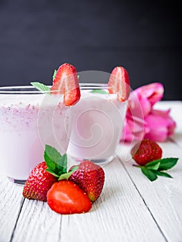 Strawberry smoothie with berries and pink flowers on white wood table and dark background. Fresh milkshake