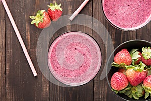 Strawberry smoothie and fresh strawberries in glass on wooden ba