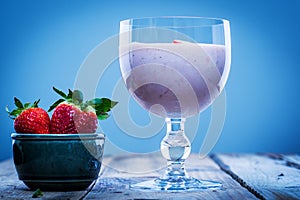 Strawberry smoothie in a glass with fresh strawberries in a bowl aside