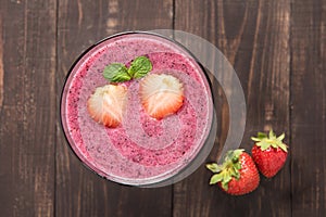 Strawberry smoothie in glass and fresh strawberries on wooden ba