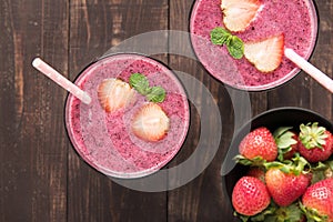 Strawberry smoothie in glass and fresh strawberries on wooden ba