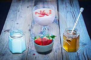 Strawberry smoothie ingredients: fresh strwawberries in a bowl, honey and yogurt in jars