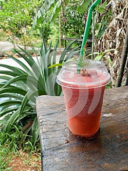 Strawberry smoothie in a plastic cup on a wooden table in the garden of a roadside cafe.