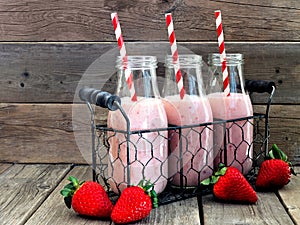 Strawberry smoothies in milk bottles against a rustic wood background