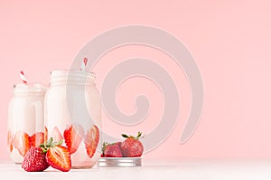 Strawberry smoothies in retro glass jars with bright sliced berries, straws on light, soft, pink background, copy space.