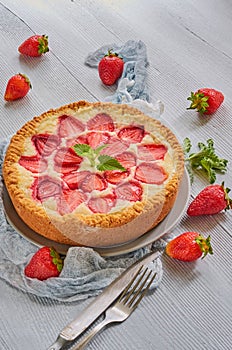Strawberry tart on the gray kitchen background. Berries cheesecake decorated with organic fresh strawberries and mint leaves