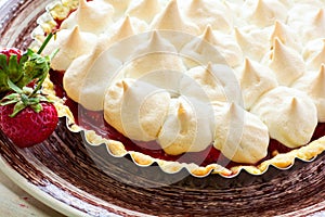 Strawberry tart with meringue on brown plate.
